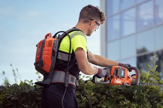 庭の環境でバックパックのバッテリーでヘッジトリマーを使用している人。