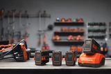 Комплект батерии Husqvarna и зарядно устройство на работна маса, с инструменти, висящи на заден план.