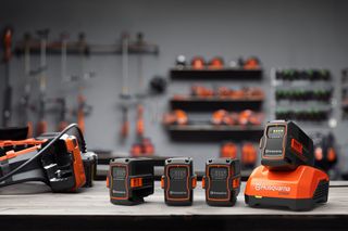 A set of Husqvarna batteries and a charger on a workbench, with tools hanging in the background.