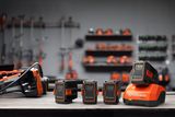 Un set di batterie Husqvarna e un caricabatterie su un banco da lavoro, con gli attrezzi appesi sullo sfondo.