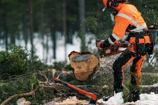 Henkilö, joka käyttää moottorisahaa tukin leikkaamiseen lumisessa metsässä.