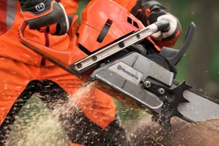 X-CUT™ C85 チゼル 3/8" 1.5mm. ハスクバーナのチェーンソーを使って丸太を切断し、木片が飛び散る人。