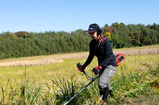 作業用具を着て草原で割草機を使う人。