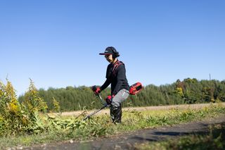 木々が背景に見える野原で、割草機を使う人。