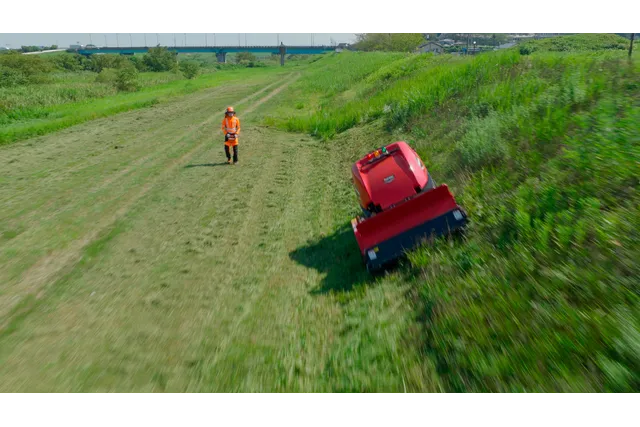 ラジコンハンマナイフモア ZHM1550RR-RC (RC KIT). 草の斜面を歩く人と、ロボットの芝刈り機が坂道で動いています。