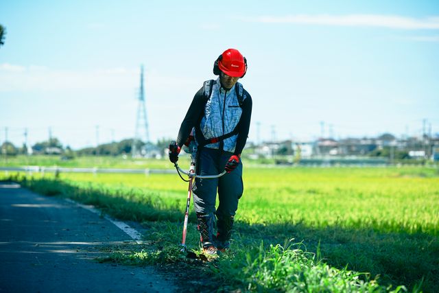 田舎の道路の端に沿って草刈り機を使用している人。