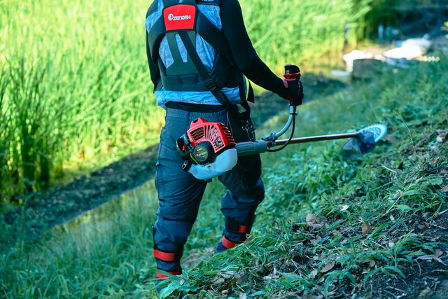 トリマーを使って水域近くの斜面で草を刈る人。
