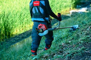 トリマーを使って水域近くの斜面で草を刈る人。