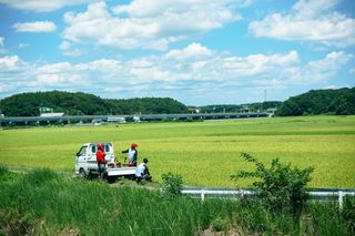 高速道路を背景に田舎の野原で小型トラックの横に立っている3人。